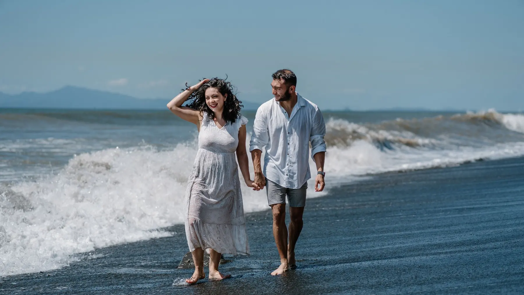 A couple walking hand in hand through the shallows on a sunny beach